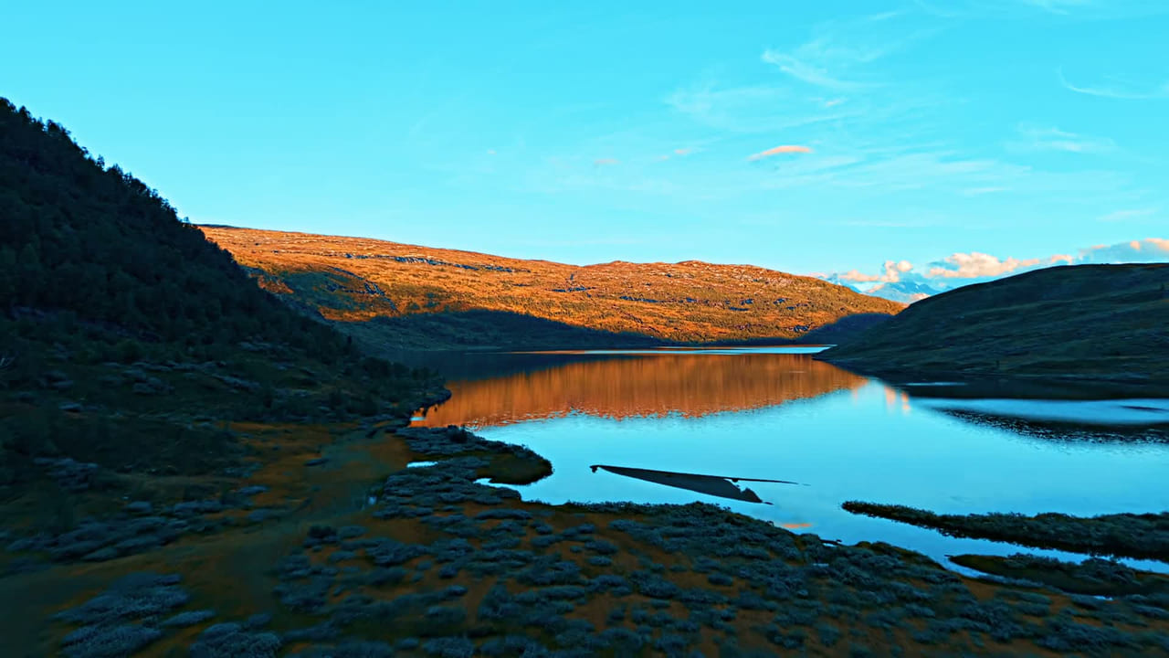 Aerial view of a mountain lake in Norway at golden hour, with sunlit hills reflected in the water